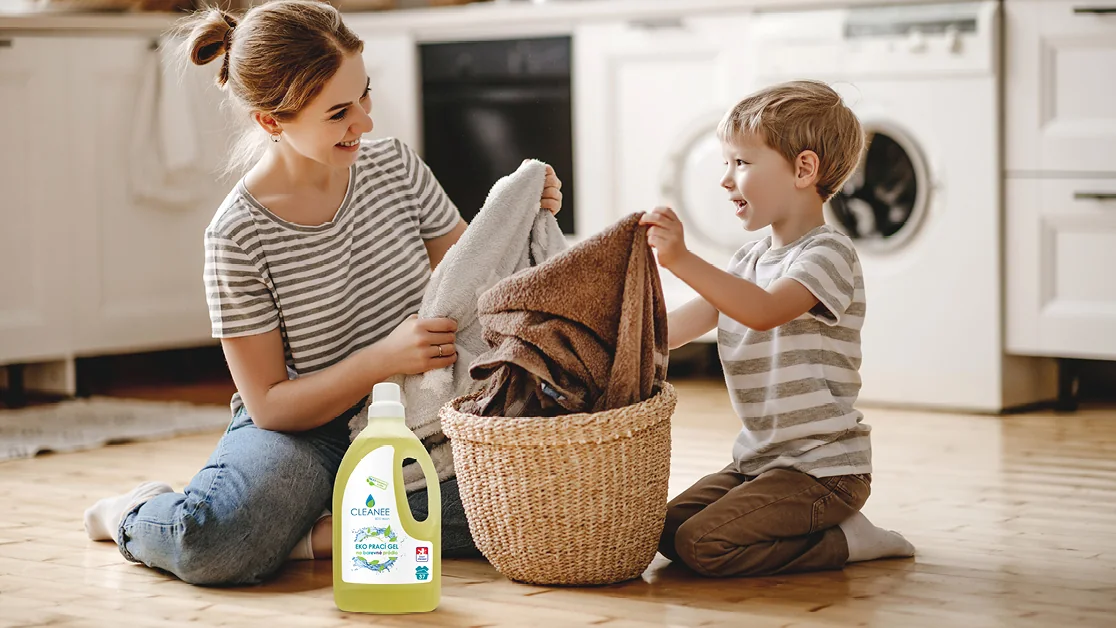 Máma se synem u pračky třídí vyprané prádlo, vedle lahev pracího gelu CLEANEE na barevné prádlo 1,5 l